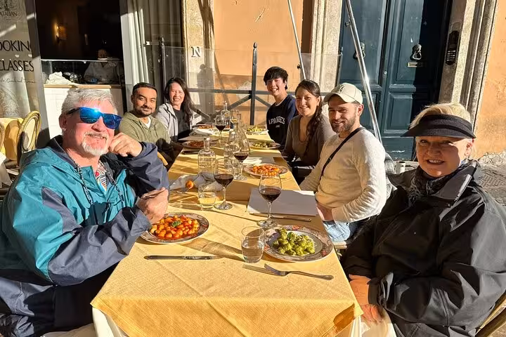 Happy participants enjoying homemade gnocchi and wine at an outdoor table during a cooking class in Rome's Piazza Navona.
