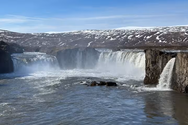 Breathtaking view of Godafoss Waterfall with snow-capped mountains, ideal for a day tour from Akureyri.