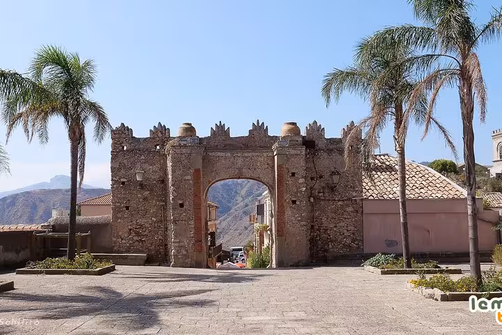 The ancient gate of Savoca, a picturesque filming location from The Godfather tour, framed by palm trees and mountain views.