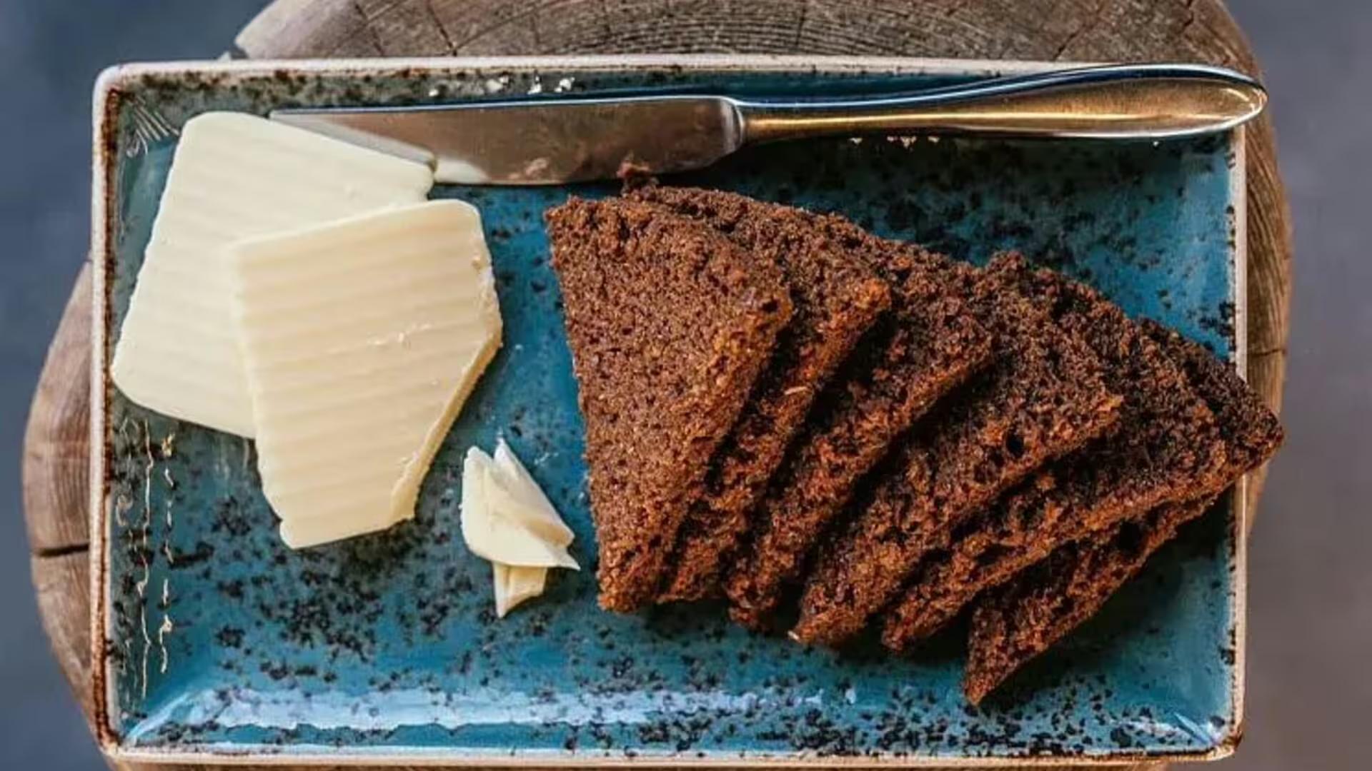 Sliced dark rye bread with butter pats and knife on blue ceramic plate