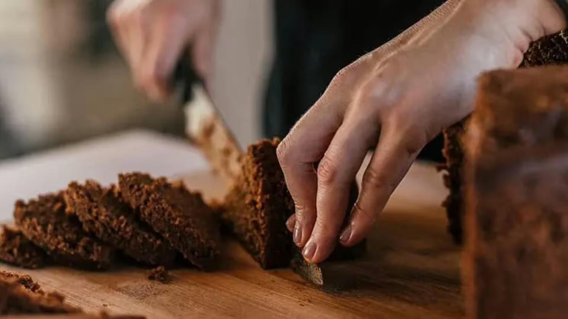 Hands slicing fresh dark rye bread on a wooden cutting board