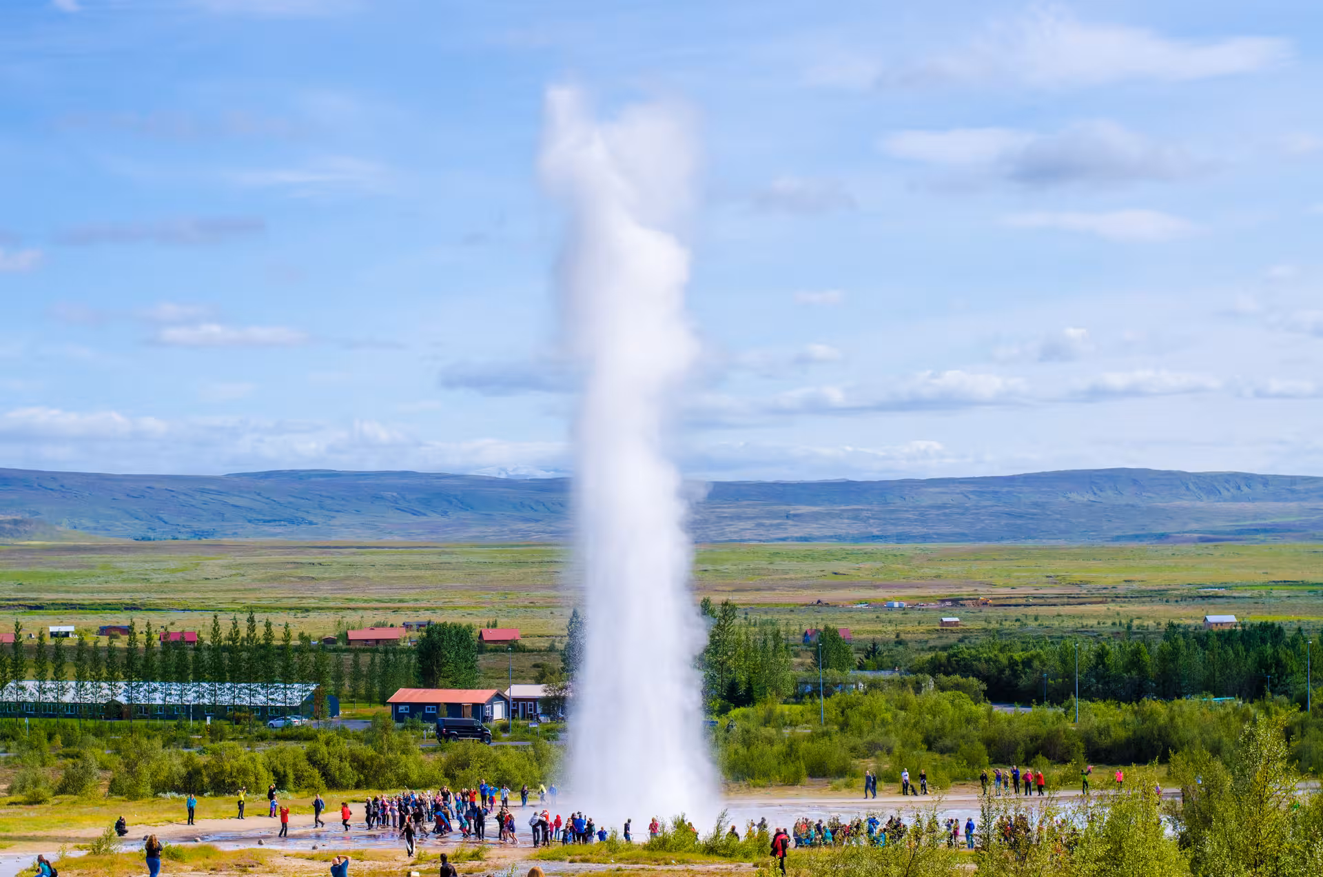Tourists admire the erupting geyser amid lush landscapes on the Private Golden Circle Super Truck 4x4 tour.