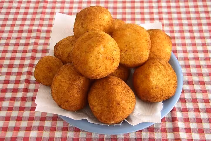 Plate of golden, crispy arancini on a red checkered tablecloth, showcasing the essence of Catania street food.