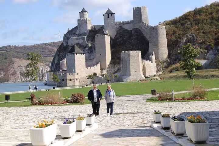 Visitors walking towards the historic Golubac Fortress, set against a backdrop of rolling hills and the Danube River.