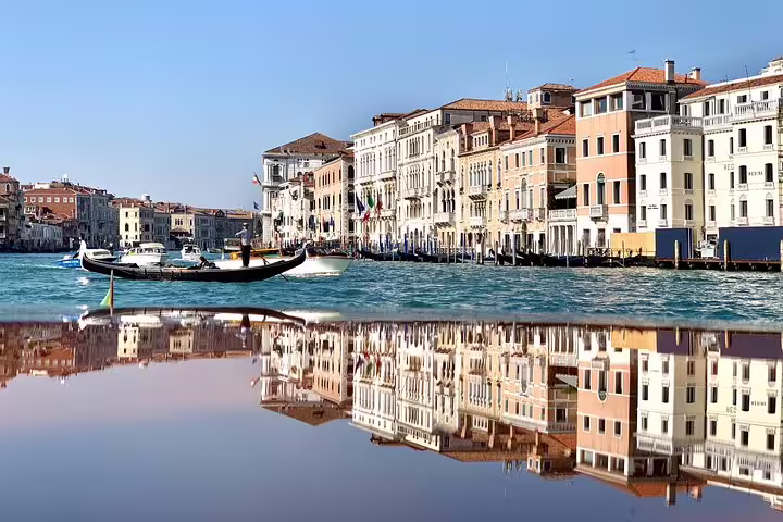 Gondola glides along Venice's Grand Canal with historic buildings reflecting in the water, perfect for a shared boat tour.