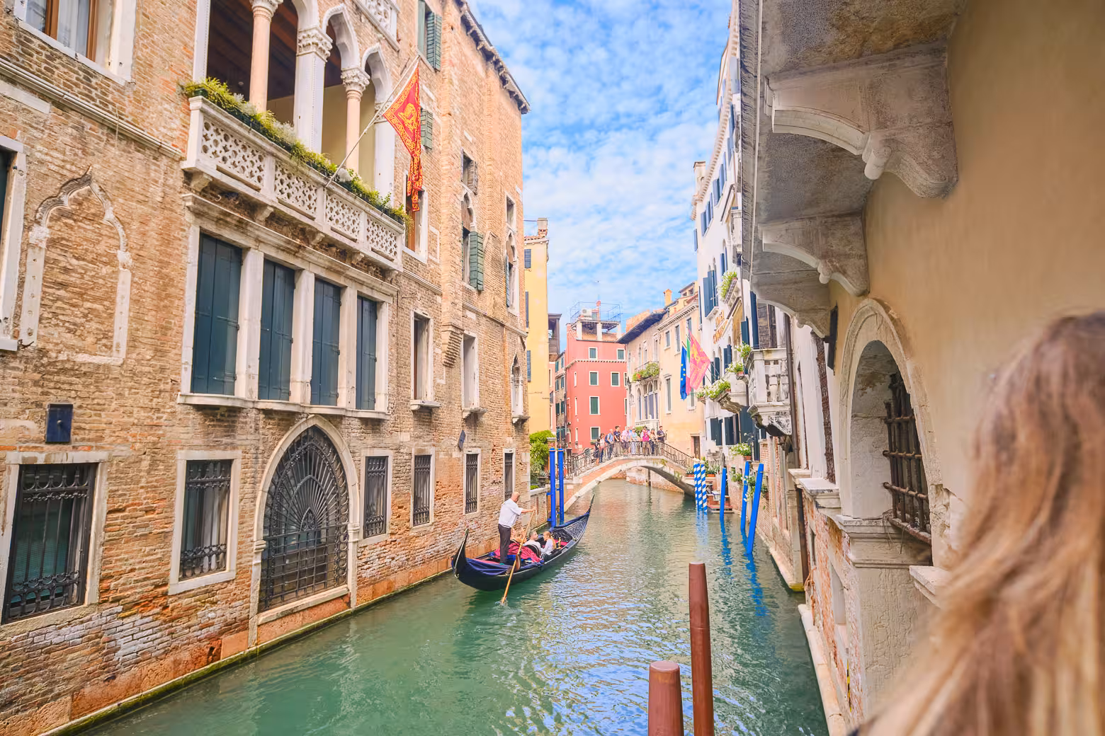 Traditional gondola glides through a picturesque Venetian canal, framed by historic buildings and arched bridges.
