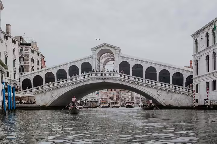 Gondolas glide under Venice's iconic Rialto Bridge on the Grand Canal, a highlight of shared tours from Piazzale Roma.