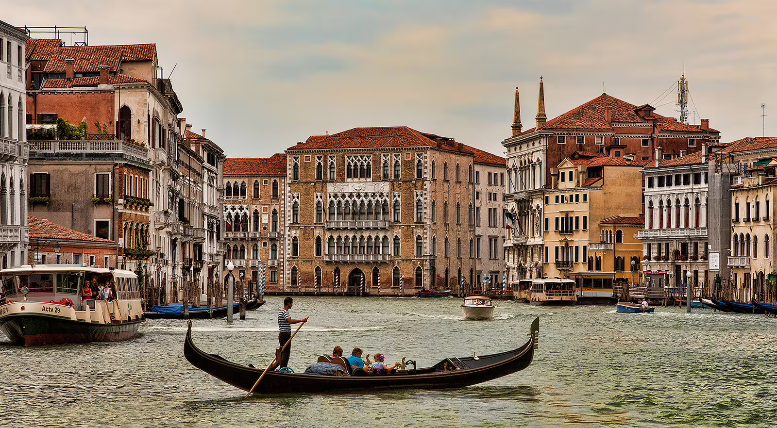 Gondolier steering a traditional gondola along Venice Grand Canal past historic palaces on a guided walking tour and boat ride