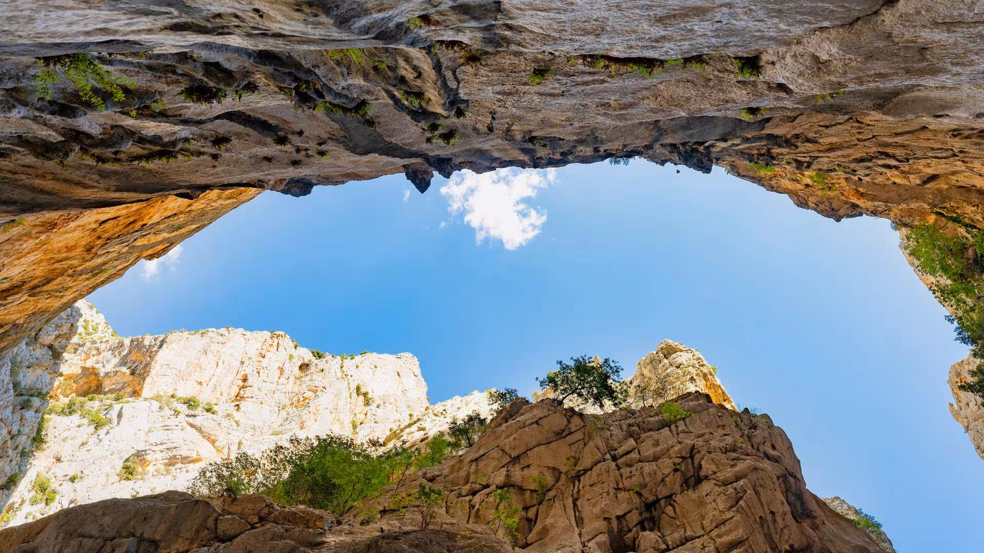 Upward view of a clear blue sky framed by towering cliffs in Gorropu Canyon, perfect for an adventurous trekking experience.