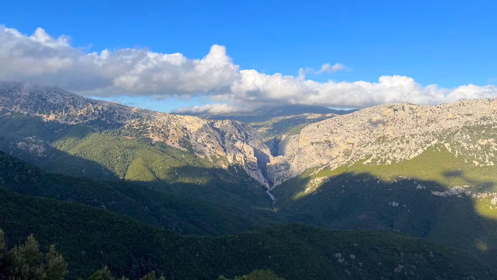 Stunning view of Gorropu Canyon nestled between lush green hills under a vibrant blue sky in Sardinia.