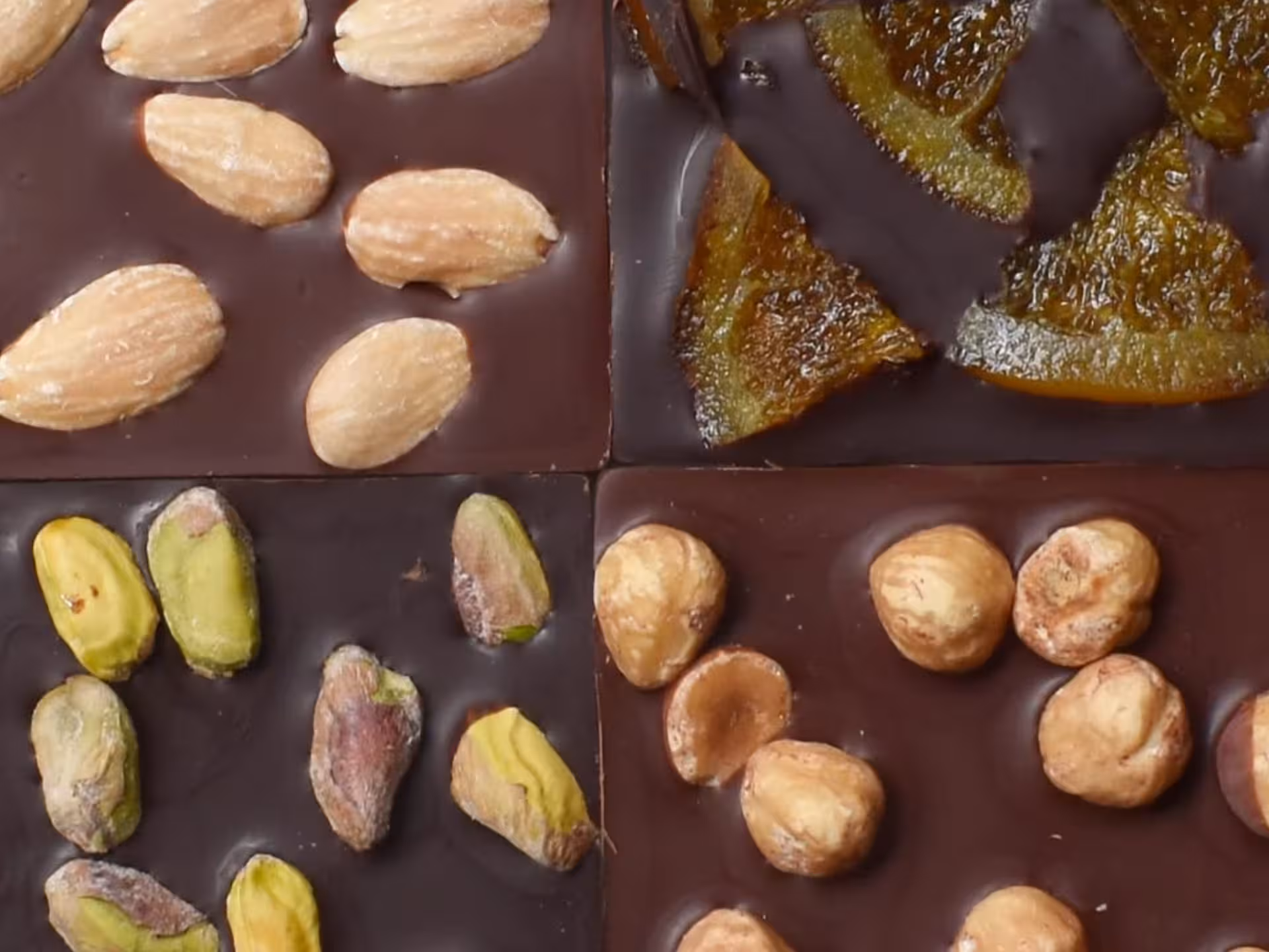 Close-up of gourmet chocolate bars topped with almonds, pistachios, candied fruit, and hazelnuts.