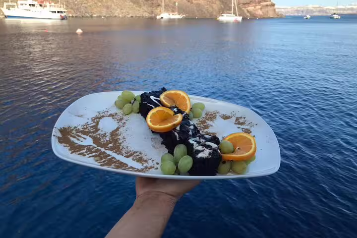 Gourmet dessert with oranges and grapes served on a catamaran cruise in Santorini's beautiful blue waters.