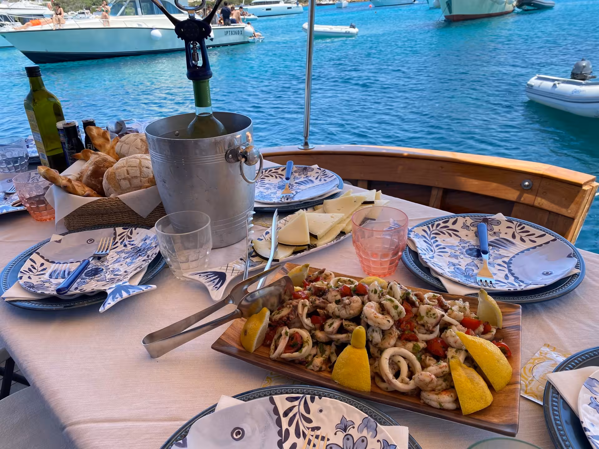 Gourmet seafood lunch with wine on a wooden boat, set against the scenic backdrop of La Maddalena waters.