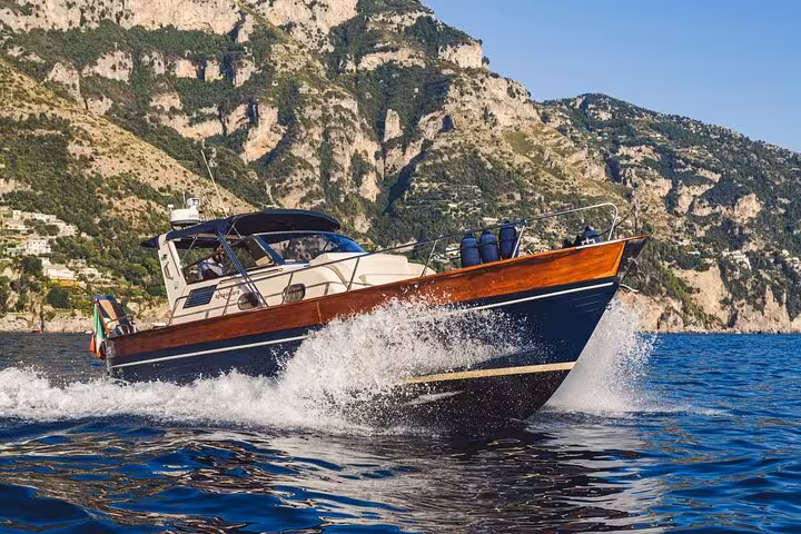 Gozzo Apreamare boat speeding through waves with scenic cliffs in the background on a Capri and Positano tour.