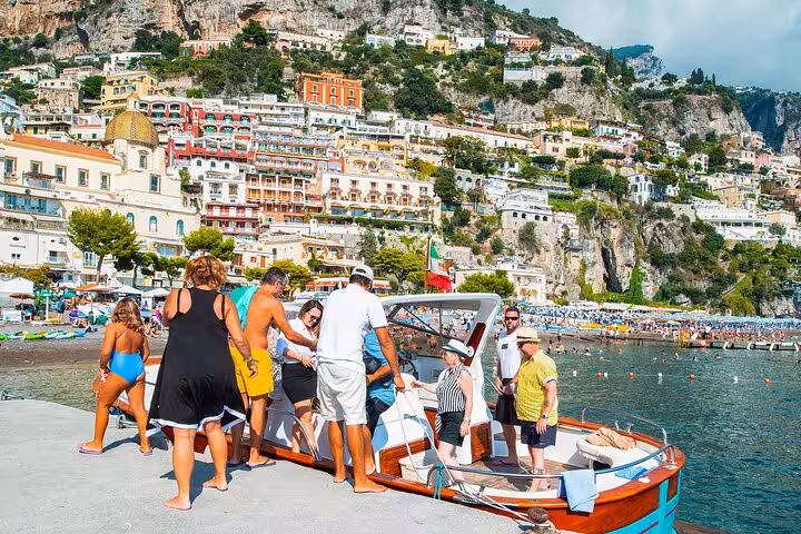 Tourists boarding a Classic Gozzo boat at the vibrant Positano harbor, surrounded by colorful cliffside buildings.