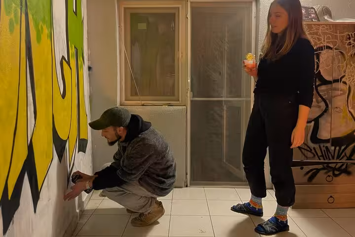 Artist paints yellow graffiti while guest sips a cocktail at Sip and Spray with locals street art experience