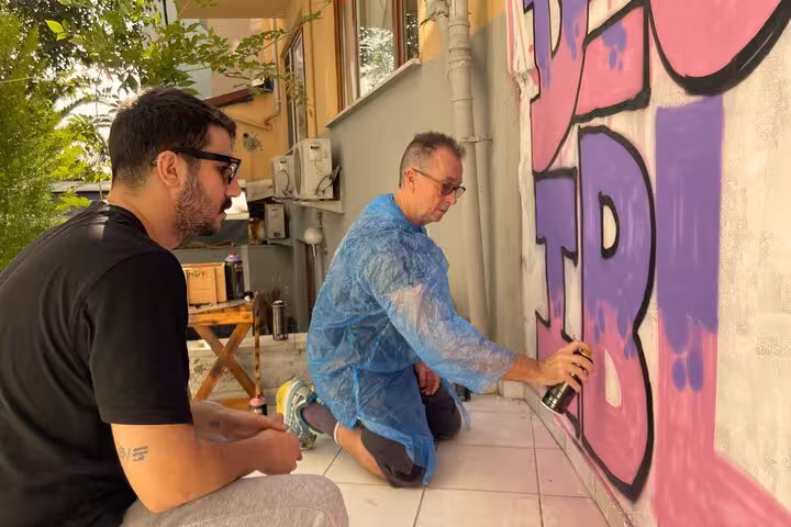 Participants spray-paint a colorful graffiti mural with a local artist during Sip and Spray cocktail tour