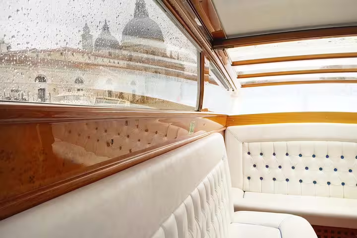Luxurious interior of a boat with rain-streaked windows, showcasing Venice architecture during the Grand Canal tour.