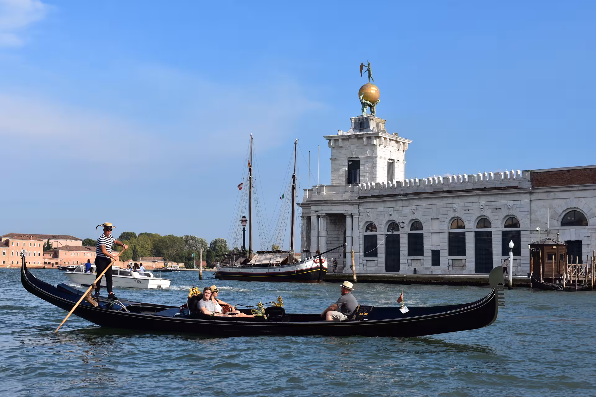 Tourists enjoying a serene gondola ride on Venice's Grand Canal with iconic landmarks and clear skies.