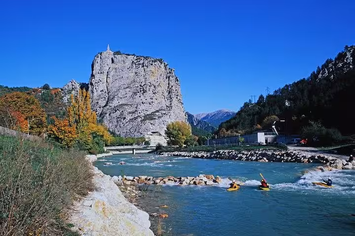 Kayakers navigate the turquoise river with towering cliffs in the Grand Canyon of Europe under a clear blue sky.