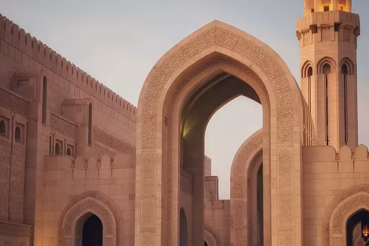 Grand Mosque archway in Muscat at dusk, showcasing intricate Islamic architecture on an evening sightseeing taxi tour