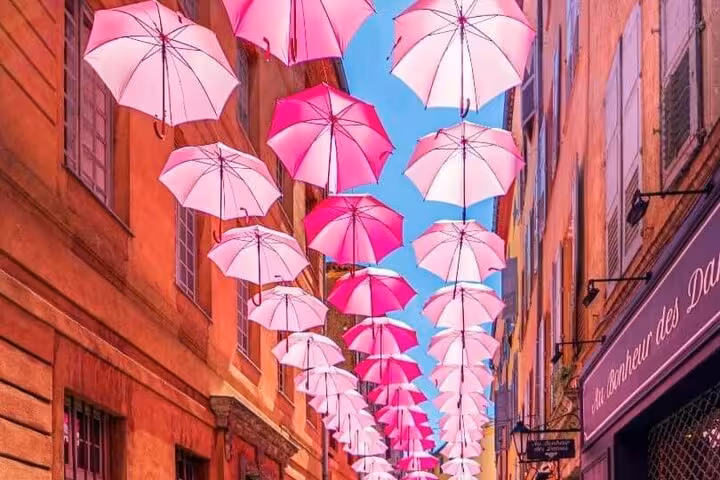 Charming Grasse street adorned with a vibrant display of hanging pink umbrellas, capturing the town's artistic flair.
