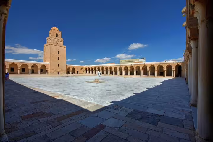 Visit the historic Great Mosque of Kairouan featuring a spacious courtyard and iconic minaret under a clear blue sky.