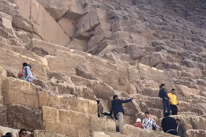 Visitors climb massive limestone blocks at the Great Pyramid on a Pyramids of Giza private tour with lunch