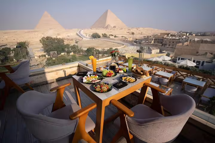 Great Pyramid Inn rooftop dinner table with drinks and mezze overlooking Giza Pyramids at sunset, Cairo