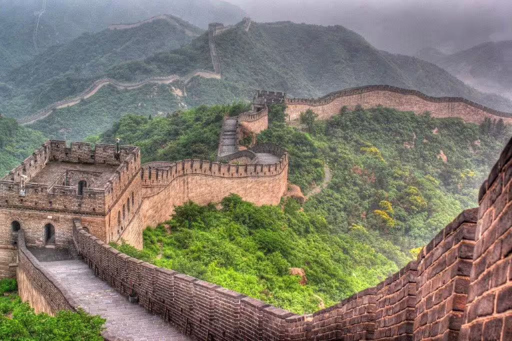 Scenic view of the Great Wall of China winding through lush green mountains on a misty day, highlighting Beijing's heritage.