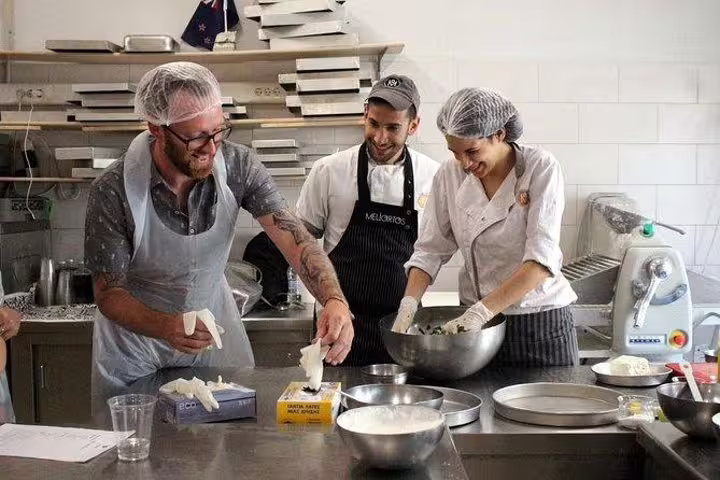 Hands-on Greek cooking class in Athens kitchen as chefs guide guests mixing ingredients before rooftop dinner