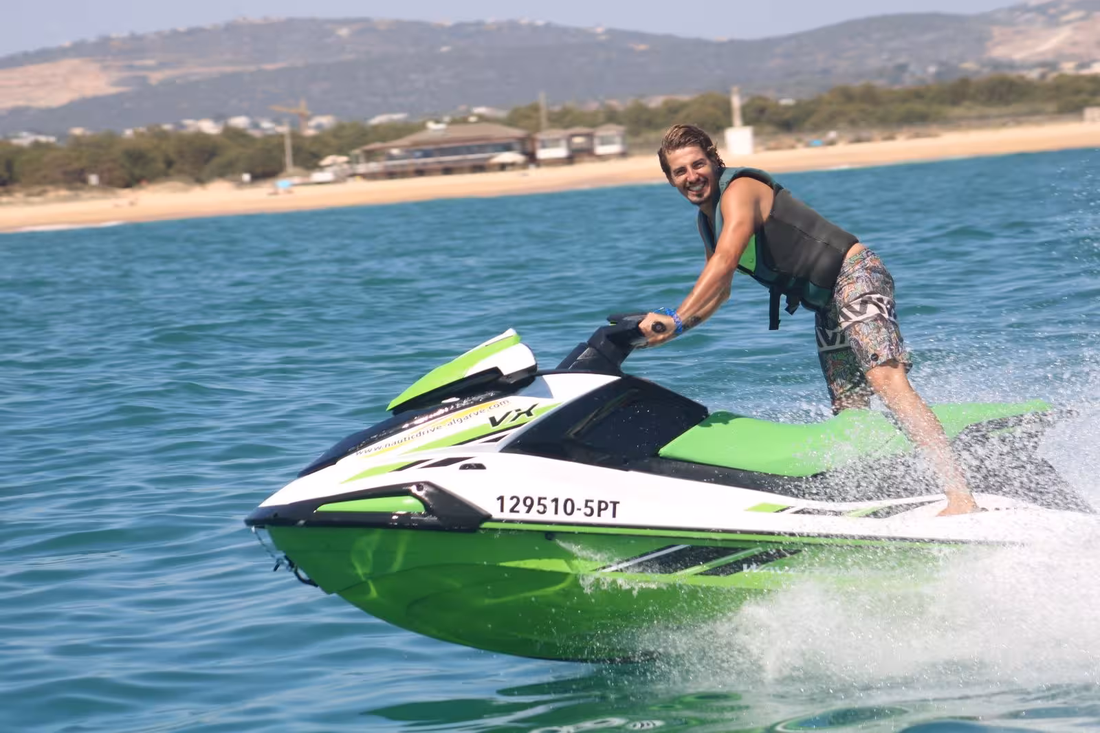 Smiling rider speeding on a green jet ski at Praia da Rocha Baixinha, enjoying Algarve jet ski rental adventure
