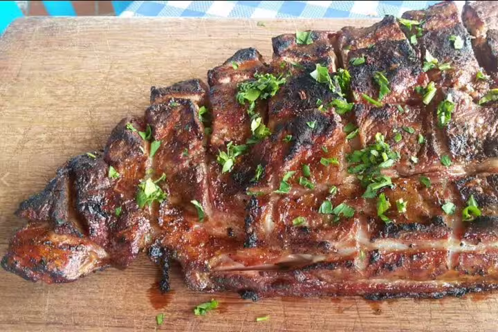 Grilled beef ribs garnished with fresh herbs on a wooden board, a highlight of Tenerife's enogastronomic tour.