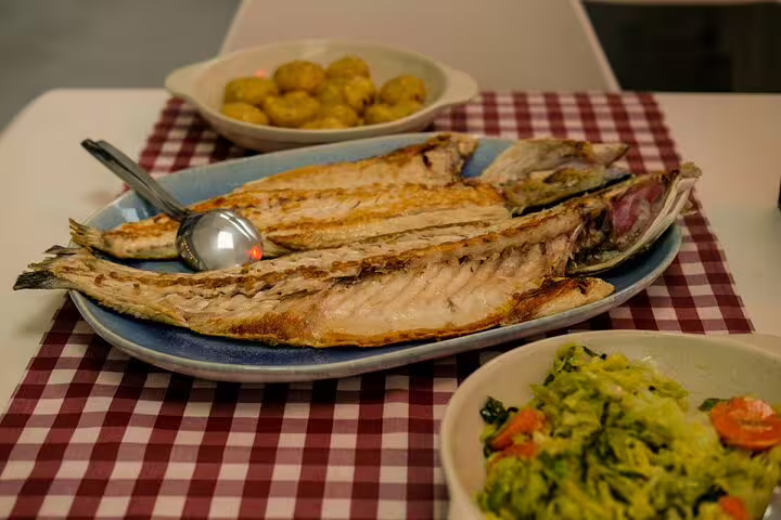 Grilled fish fillets with sides of potatoes and greens on a checkered tablecloth, showcasing a sea-to-table market tasting tour.
