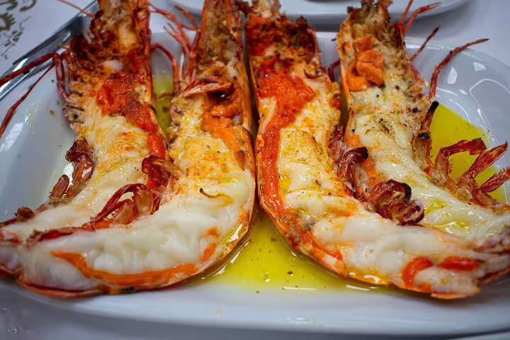 Grilled prawns drizzled with olive oil, served on a white plate, showcasing authentic Portuguese seafood cuisine on a Lisbon tour.