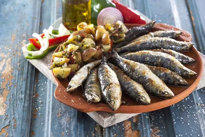 Grilled sardines with roasted vegetables on a rustic plate, a traditional dish enjoyed during the Algarve tour from Lisbon.