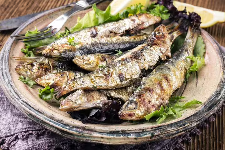 Grilled sardines served with fresh greens and lemon, showcasing a classic culinary experience on a Lisbon and Cacilhas food tour.