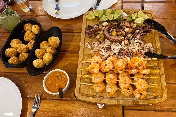 Delicious grilled seafood platter with shrimp skewers, octopus, lime wedges, and Brazilian cheese balls on wooden table.