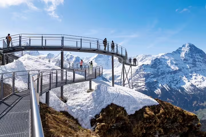 Tourists exploring a high-altitude walkway with breathtaking mountain vistas at Grindelwald First, Switzerland.