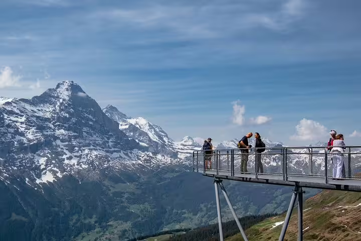 Visitors enjoying panoramic views of the snow-capped Swiss Alps from a scenic platform in Grindelwald First.