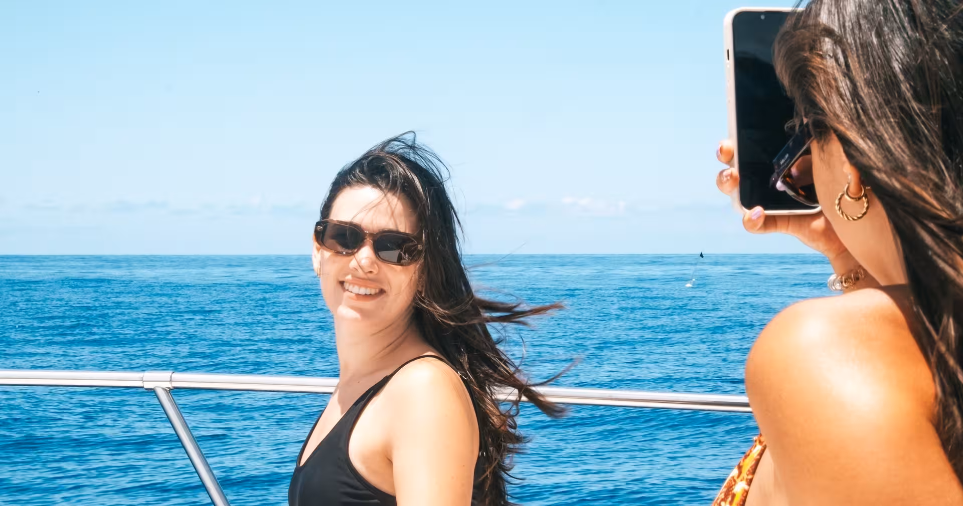 Smiling friends capturing memories on a sunny yacht cruise with endless ocean views.