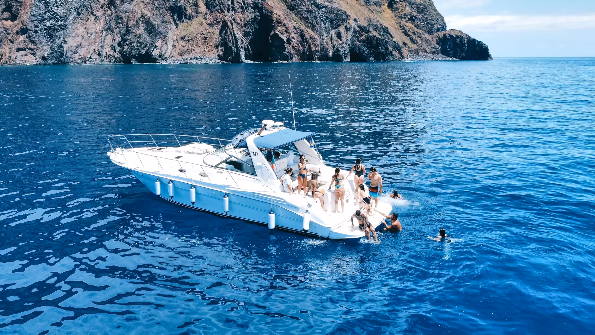 People enjoying a sunny day on the GRINGO Yacht near rocky cliffs, perfect for whale and dolphin watching adventure.