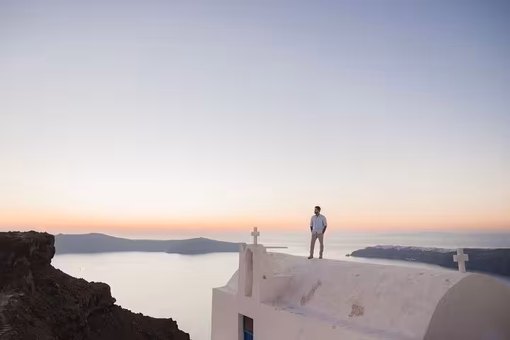 Groom on white rooftop overlooking Santorini caldera at sunset, Instagram honeymoon photo shooting tour