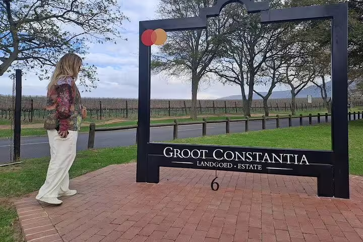 Visitor at Groot Constantia Estate entrance with scenic vineyards, highlighting Cape Town's historic wine tour.