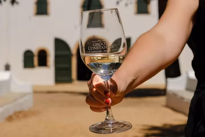 Hand holding a glass of white wine at Groot Constantia, showcasing the historic winery's elegant architecture.