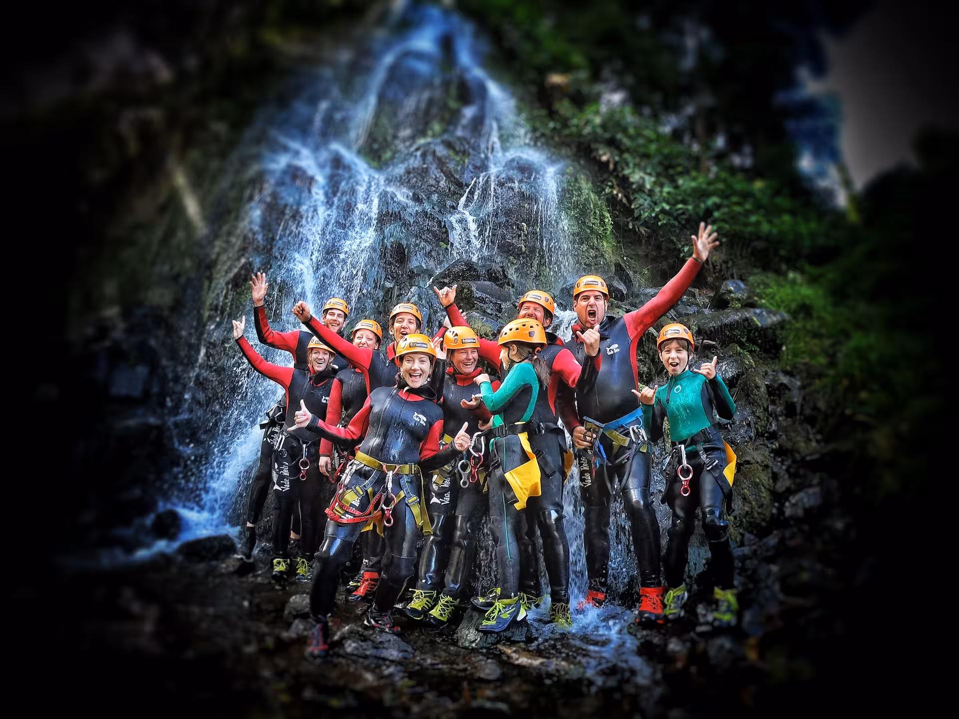 Group canyoning adventure in wetsuits and helmets cheering by a waterfall, guided outdoor experience tour