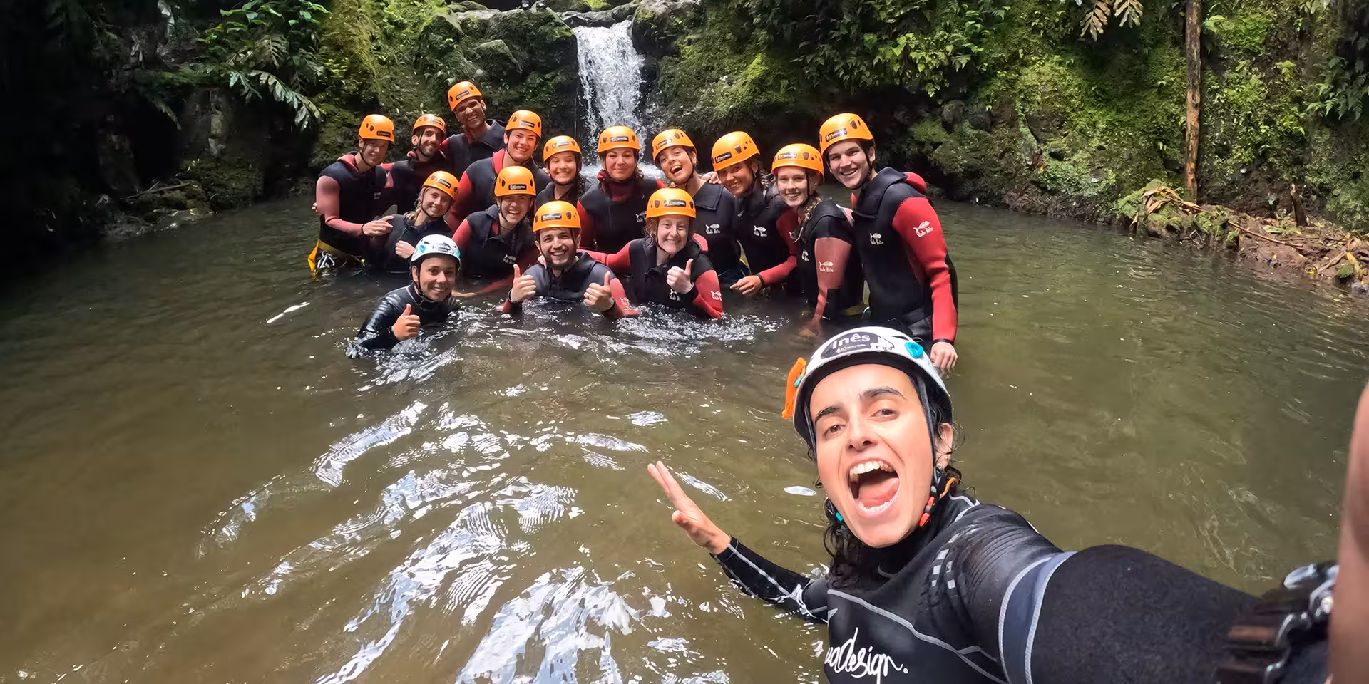 Group canyoning tour selfie in a jungle pool by a waterfall, wearing helmets and wetsuits, guided adventure
