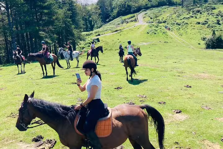 Group of people enjoying horseback riding on a lush green mountain trail, perfect for scenic adventure tours.