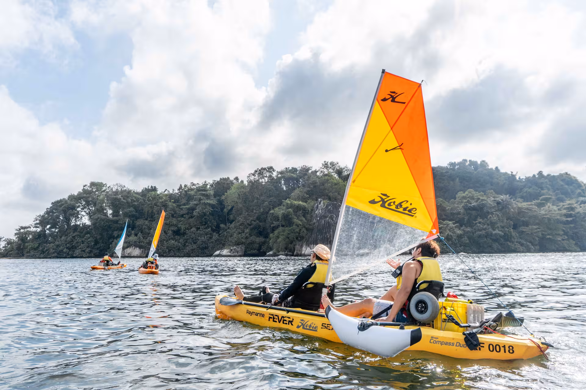 Group enjoying a kayak sailing adventure on scenic waters with lush greenery in the background.