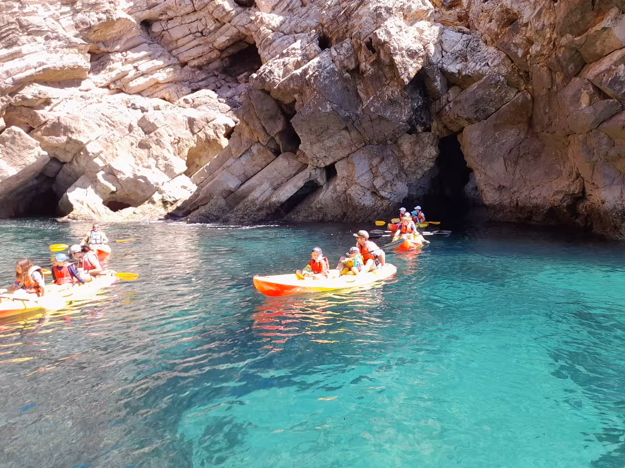 Group kayaking in clear turquoise water near rocky cliffs on guided adventure tour.